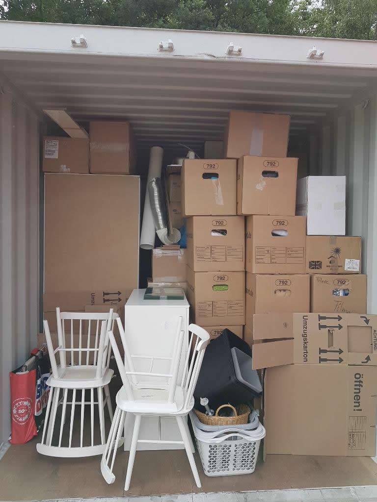 Geöffneter Lagercontainer, gefüllt mit Umzugskartons, Stühlen und Hausrat